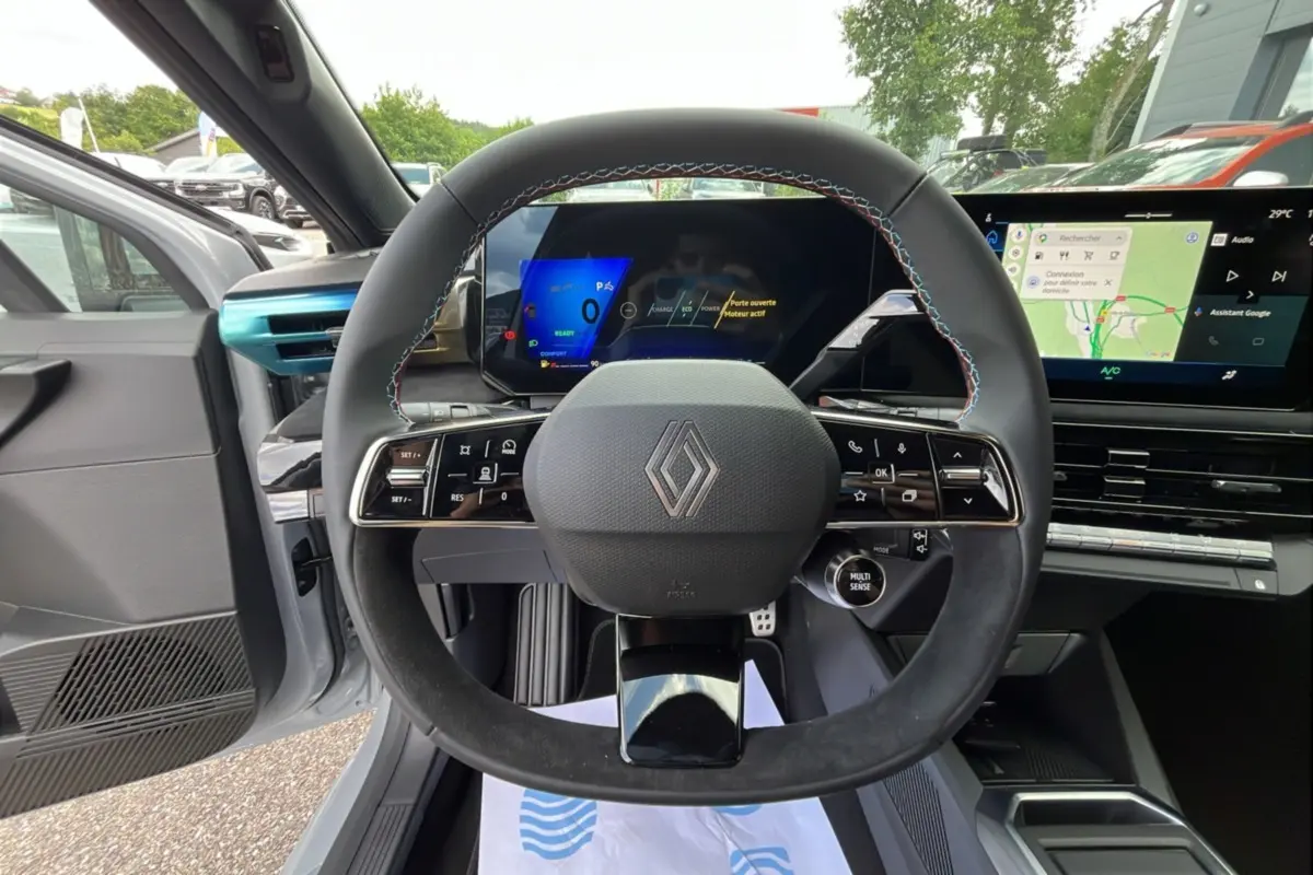 Vue intérieure centrée sur le volant cuir noir avec surpiqûres tricolores et tableau de bord numérique de la Renault Clio Gris Rafale.