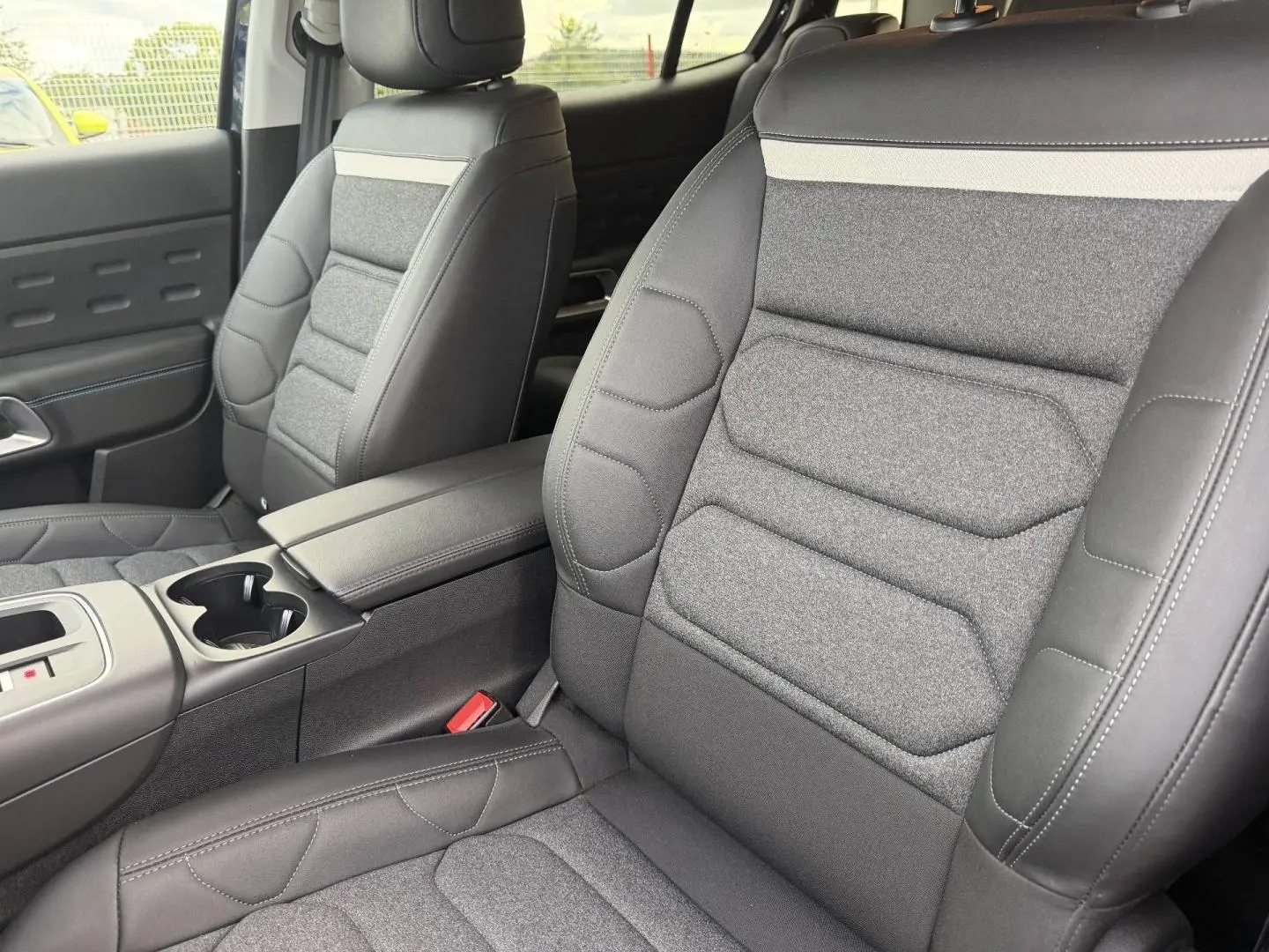 Vue intérieure rapprochée des sièges avant en tissu noir et cuir avec accoudoir central du Citroën C5 Aircross 2025.