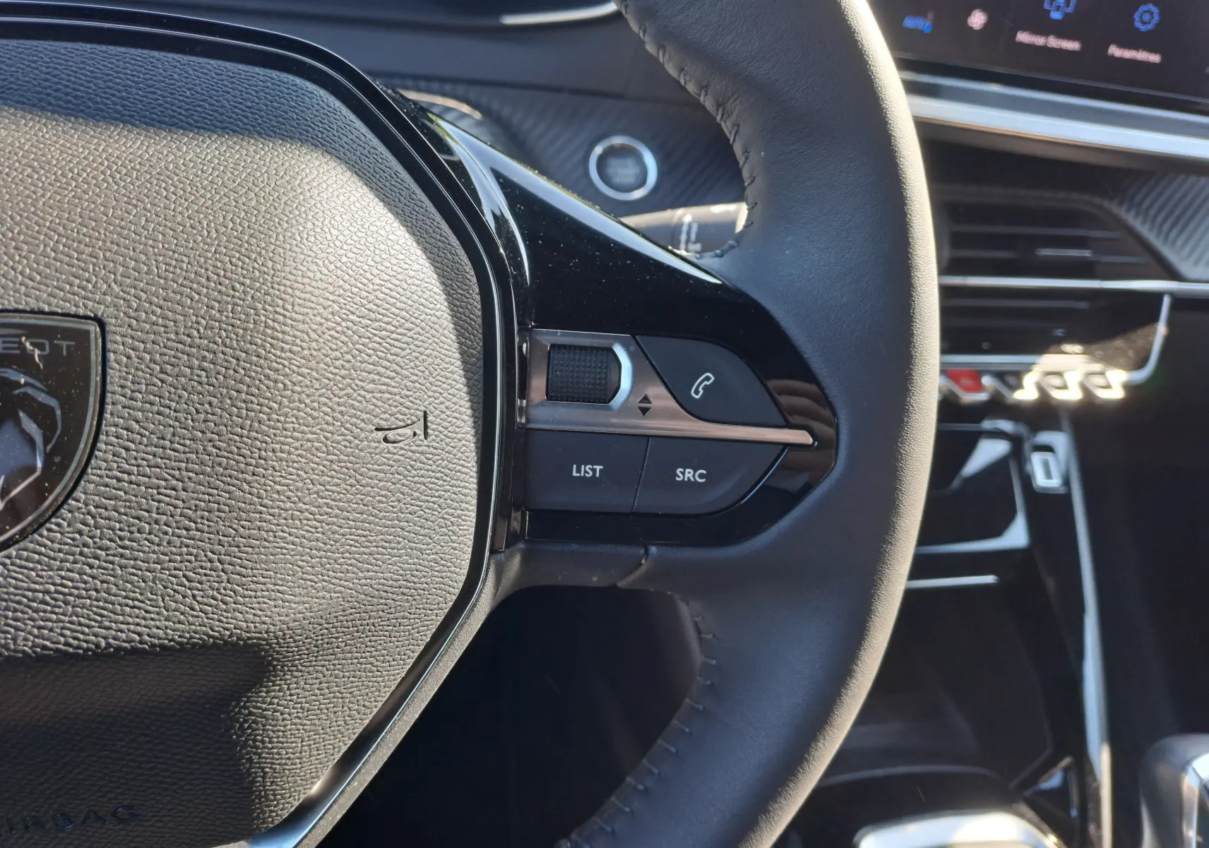 Gros plan sur le volant côté droit du Peugeot 2008 Rouge Elixir 2023, avec commandes audio et écran tactile en arrière-plan.