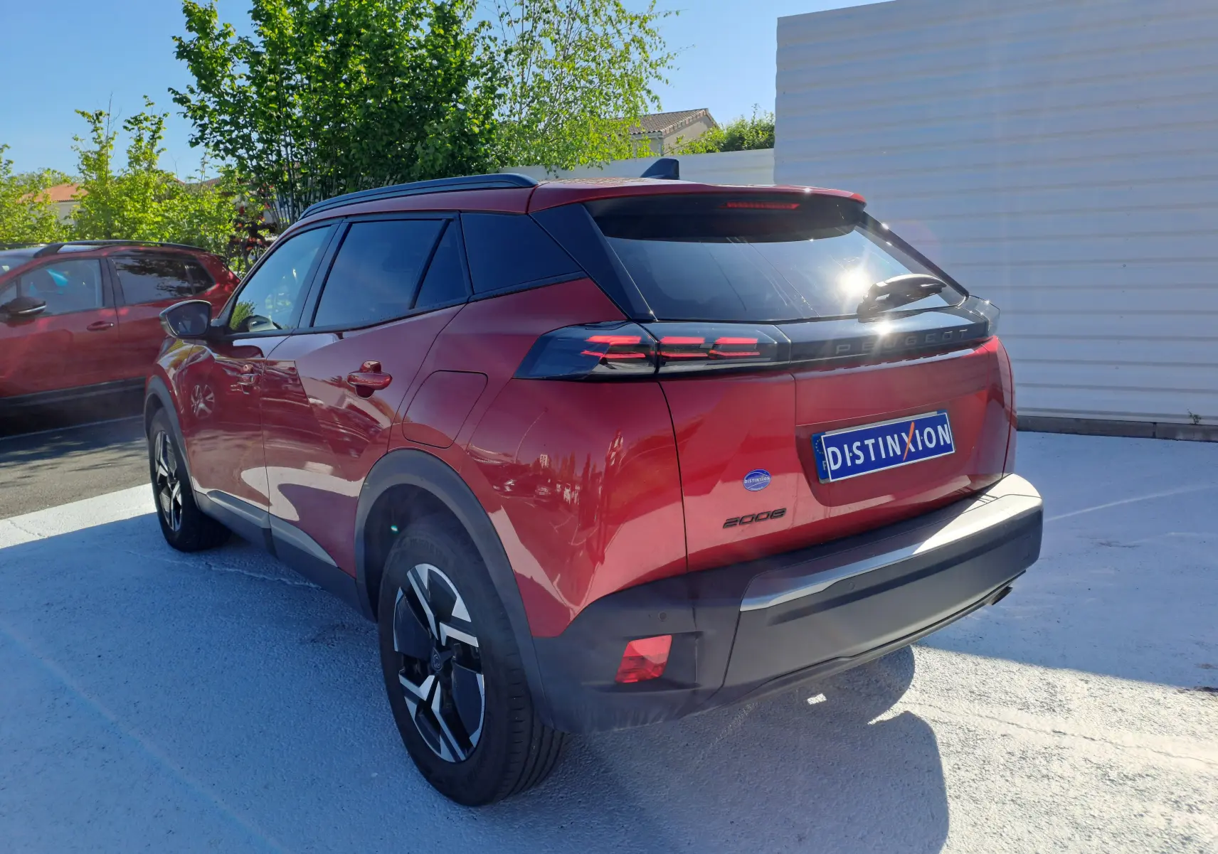Peugeot 2008 rouge Elixir vue 3/4 arrière droit, avec feux arrière LED et vitres teintées sur parking extérieur.