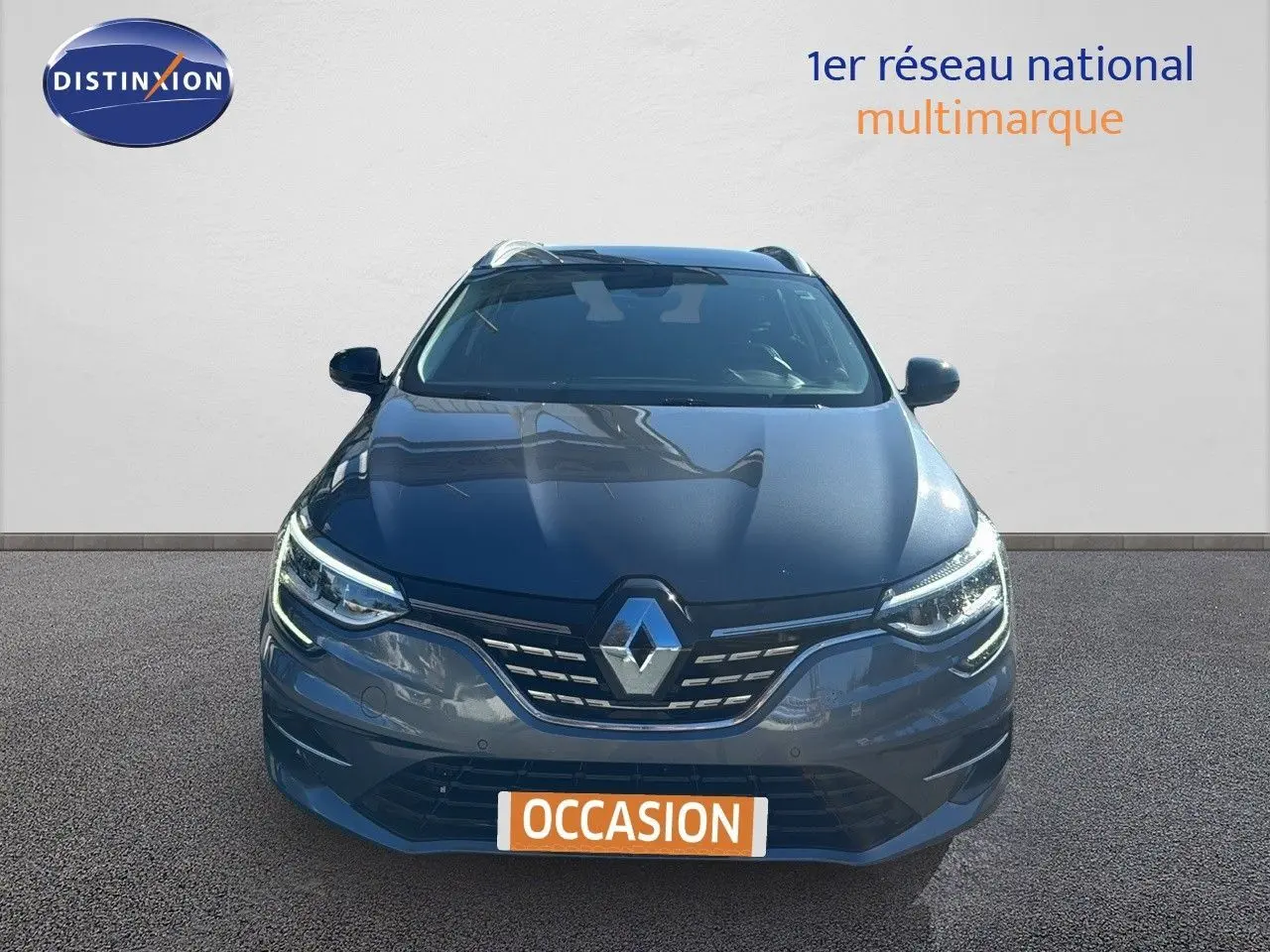 Vue avant d'une Renault Mégane Break gris titanium métal avec calandre et phares LED allumés sur fond neutre.