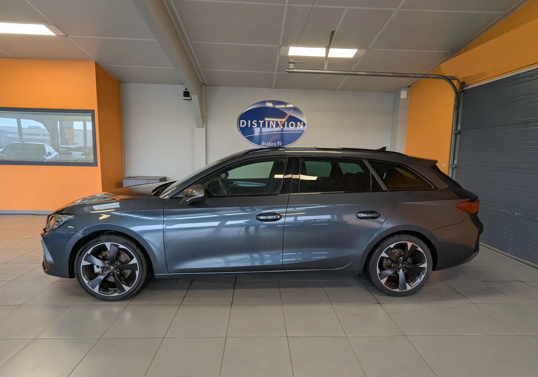 Vue de profil côté gauche d'une CUPRA LEON ST gris magnetic avec jantes alliage 18 pouces dans un showroom.