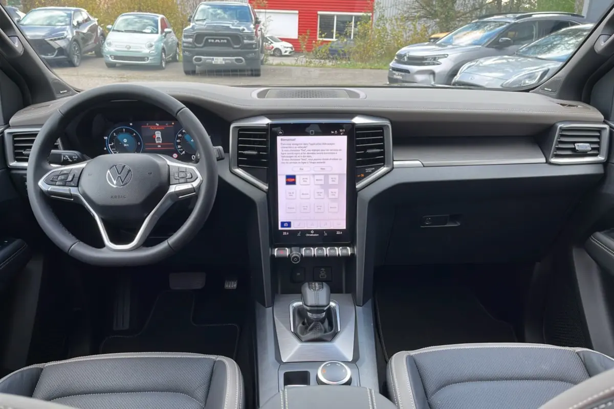 Vue intérieure avant du Volkswagen Amarok Simple Cabine 2025, tableau de bord moderne avec écran tactile vertical et volant cuir noir.