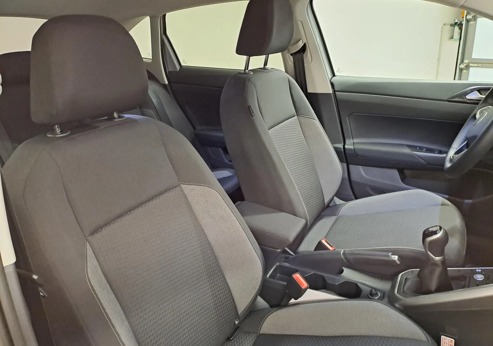 Vue intérieure des sièges avant et levier de vitesses d'un Volkswagen Taigo 2025, tissu gris foncé, boîte manuelle.