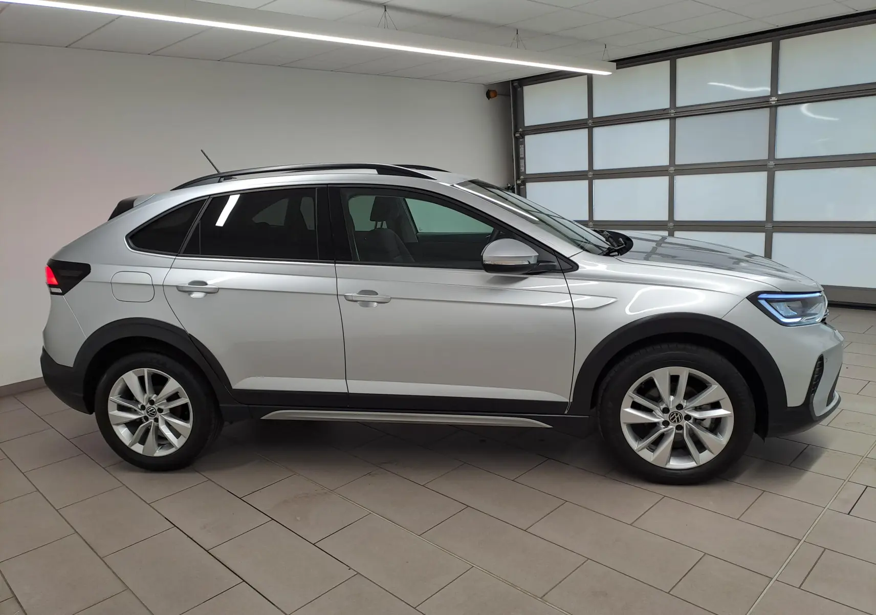 Vue de profil côté gauche du Volkswagen Taigo 2025 en peinture métallisée Reflet d'argent, avec jantes alliage et toit noir.