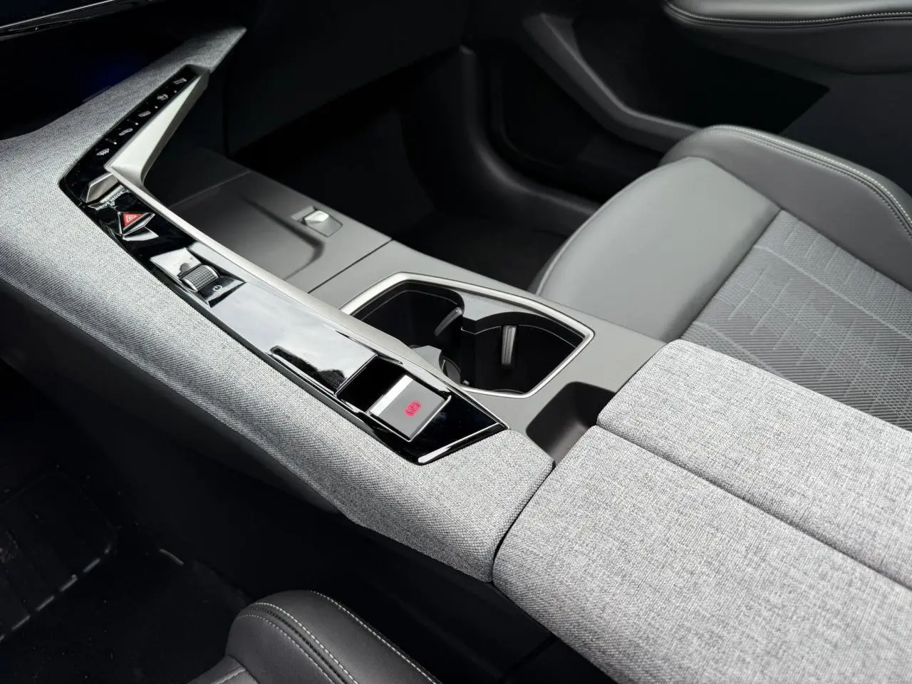 Vue rapprochée de la console centrale grise et noire du Peugeot 3008 Hybrid 145 e-DSC6 GT avec sellerie tissu et accoudoir.