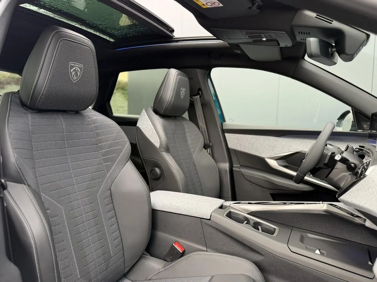 Vue intérieure côté droit du Peugeot 3008 Hybrid GT 2026, sièges tissu gris avec surpiqûres et toit ouvrant panoramique.
