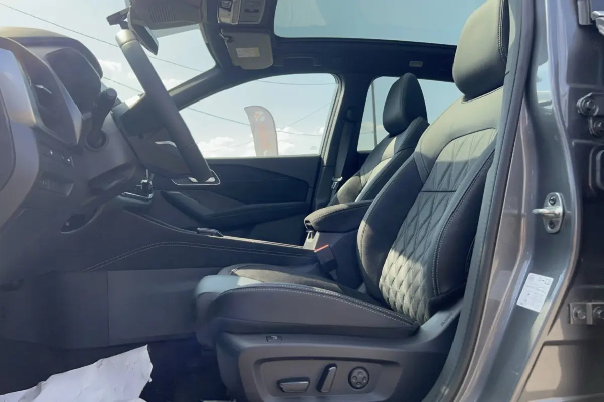 Vue intérieure côté conducteur du Nissan Qashqai E-POWER 205 Tekna Plus gris squale, sièges cuir avec surpiqûres et toit panoramique visible.