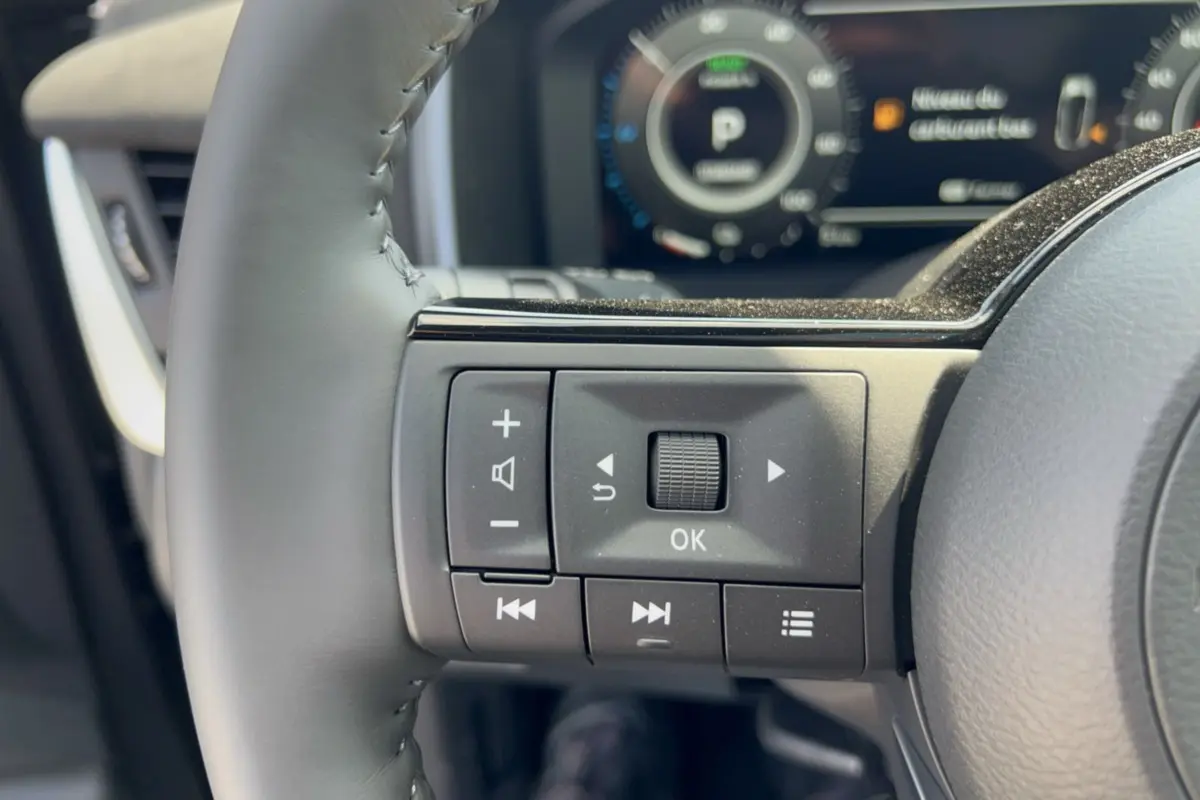 Gros plan sur les commandes multifonctions à gauche du volant cuir du Nissan Qashqai gris squale, tableau de bord en arrière-plan flou.