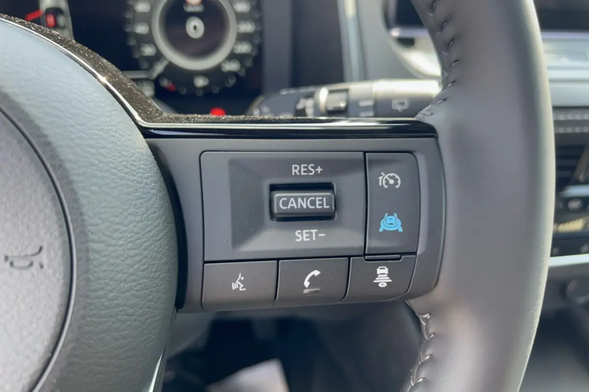 Gros plan sur les commandes multifonctions du volant cuir du Nissan Qashqai E-POWER 205 Tekna Plus, intérieur noir.