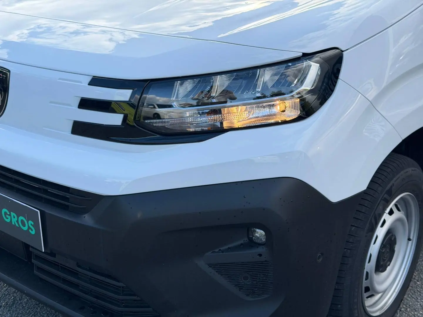 Gros plan sur l'avant droit du Peugeot Partner blanc Icy, avec phare allumé et pare-chocs noir mat.