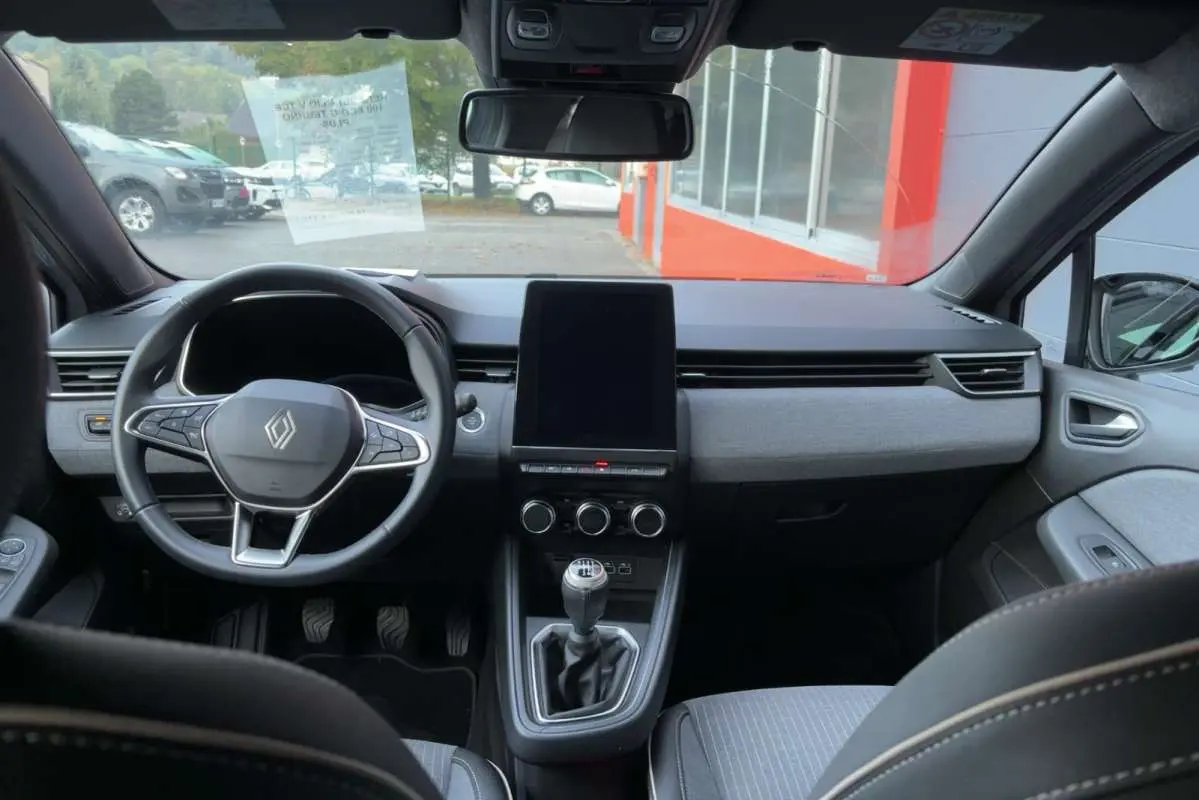Vue intérieure avant de la Renault Clio gris rafale 2025, avec volant multifonctions et écran tactile vertical central.