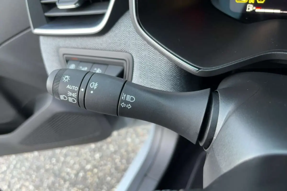 Gros plan sur la commande des feux et clignotants à gauche du volant dans l'habitacle gris de la Renault Clio 2025.