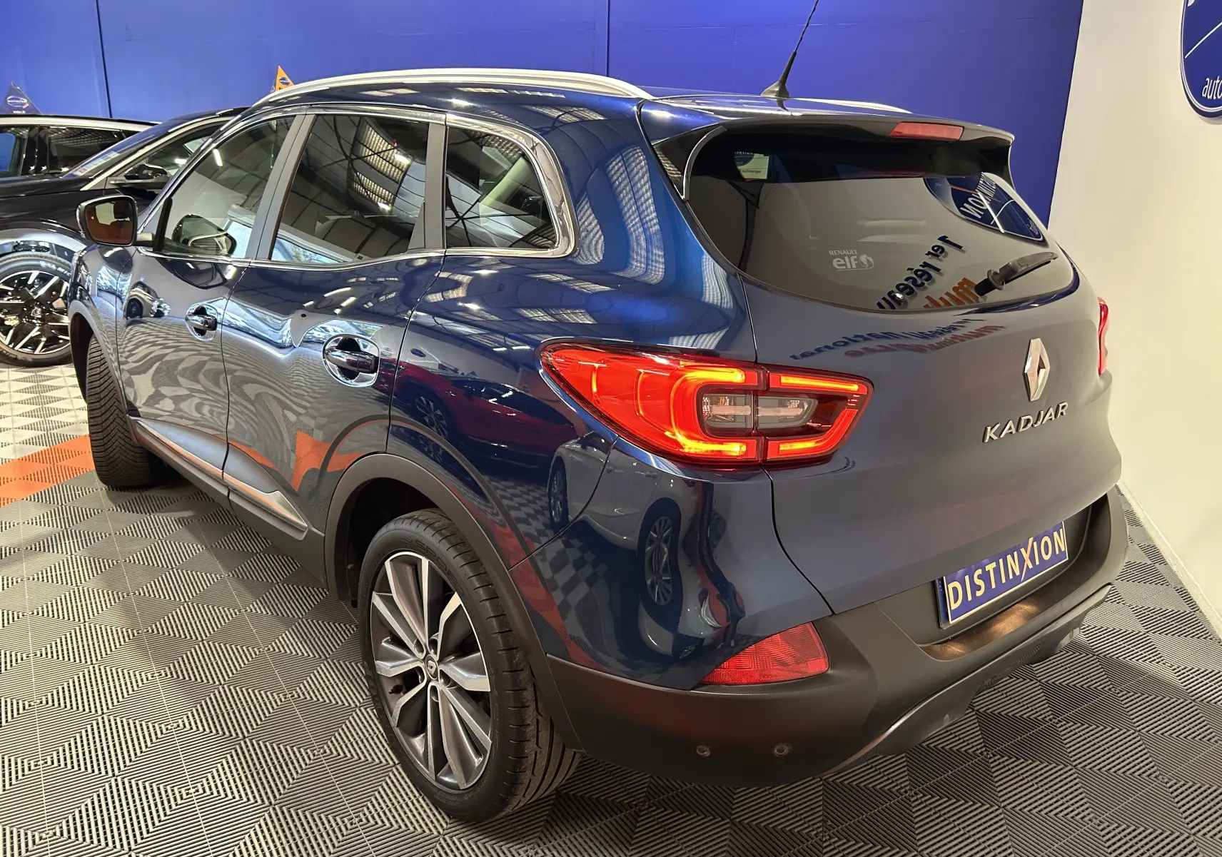 Vue 3/4 arrière droite d'un Renault Kadjar bleu 2017 avec feux arrière allumés dans un showroom.
