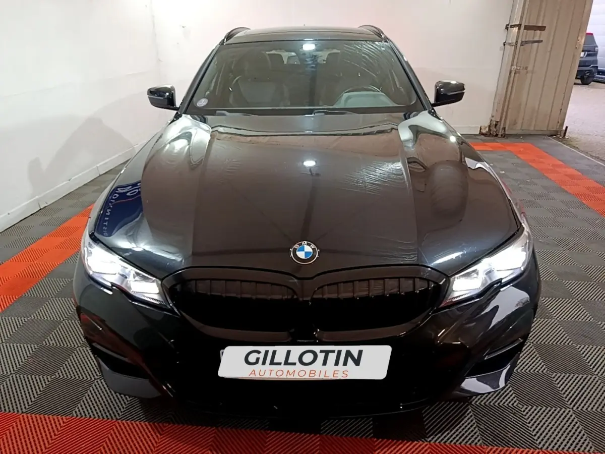 BMW Série 3 318i M Sport noir vue de face en intérieur avec calandre noire et phares LED allumés.