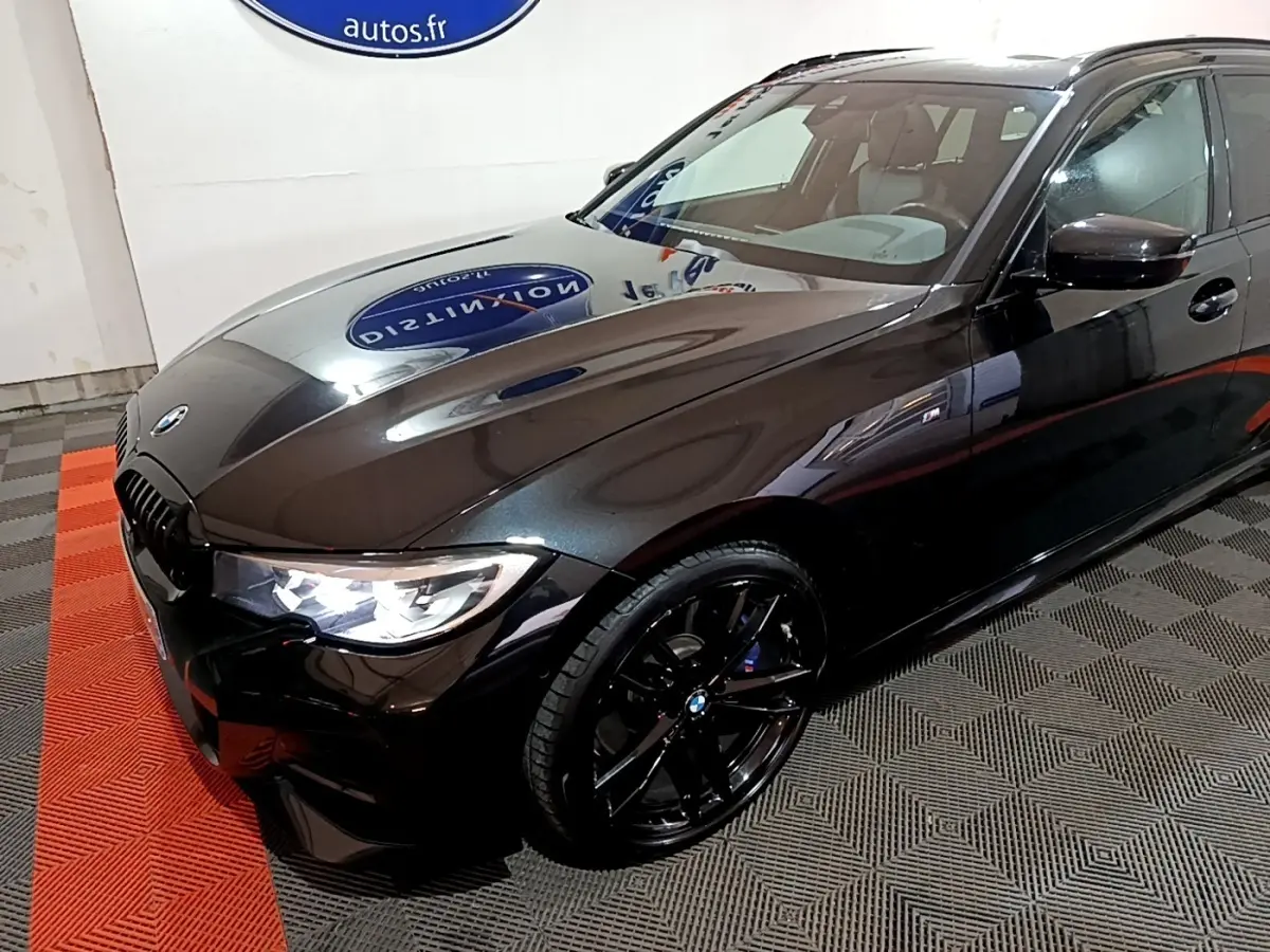 BMW Série 3 318i M Sport noir vue 3/4 avant droit avec jantes noires et phares LED allumés.