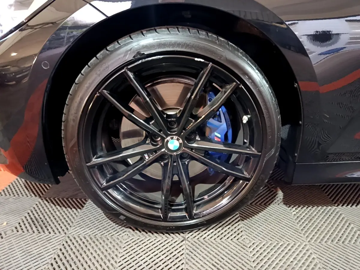 Gros plan sur la roue arrière gauche noire d'une BMW Série 3 318i M Sport avec étrier de frein bleu visible.