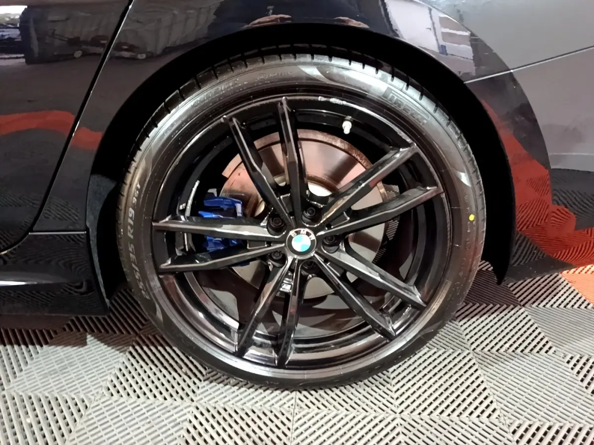 Gros plan sur la roue arrière droite noire d'une BMW Série 3 318i M Sport avec étrier de frein bleu visible.