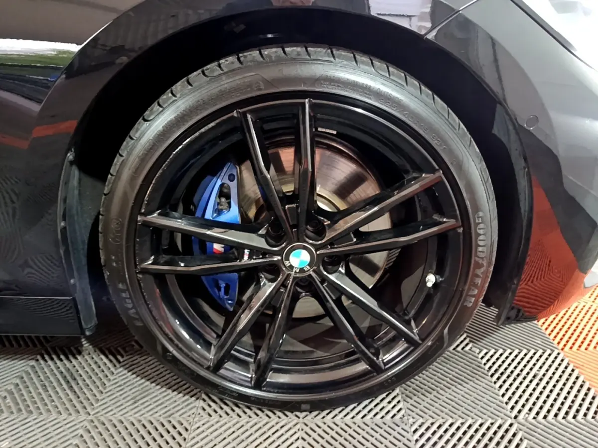 Gros plan sur la roue arrière droite noire d'une BMW Série 3 318i avec étrier de frein bleu M Sport visible.