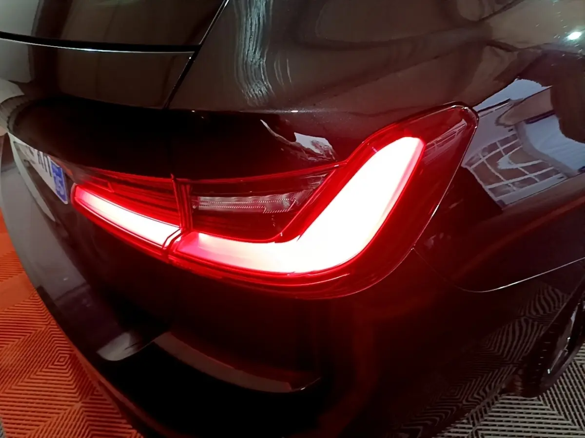 Feu arrière droit allumé d'une BMW Série 3 noire 318i M Sport, vue rapprochée du coin arrière du véhicule.