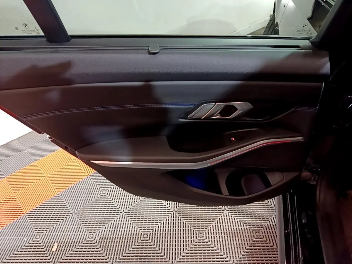 Porte intérieure côté gauche noire de BMW Série 3 318i M Sport 2022 avec éclairage d'ambiance rouge fin et poignée alu.