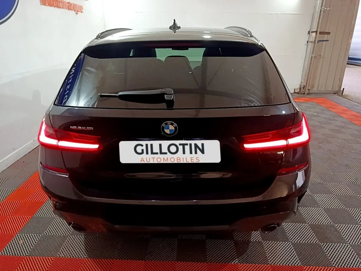 Vue arrière d'une BMW Série 3 318i noire avec feux LED allumés dans un showroom intérieur.