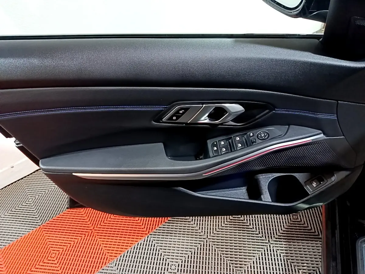 Vue rapprochée de la porte côté gauche noire de la BMW Série 3 318i M Sport avec surpiqûres bleues et commandes électriques.