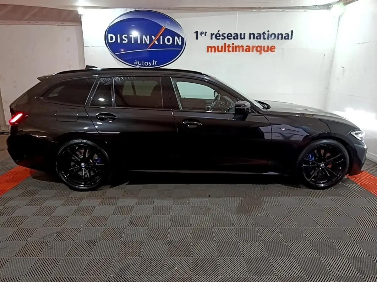 BMW Série 3 318i M Sport noir vue de profil côté gauche, avec jantes noires et feux arrière allumés.