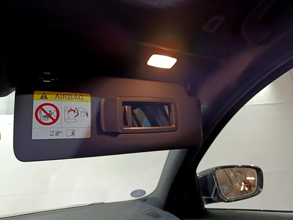 Détail du pare-soleil côté conducteur avec miroir et avertissement airbag dans une BMW Série 3 noire 2022.