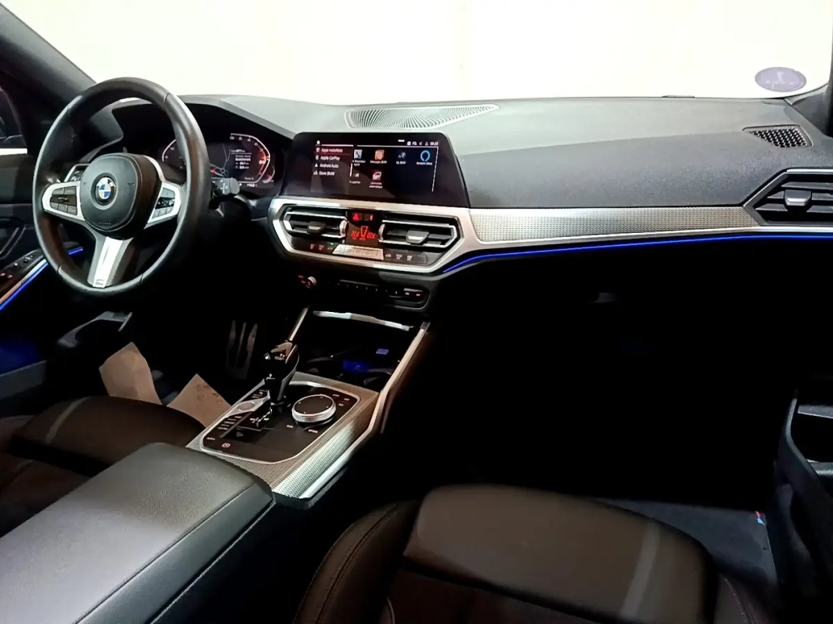 Intérieur BMW Série 3 318i 2022 vu côté conducteur, tableau de bord moderne avec éclairage d'ambiance bleu