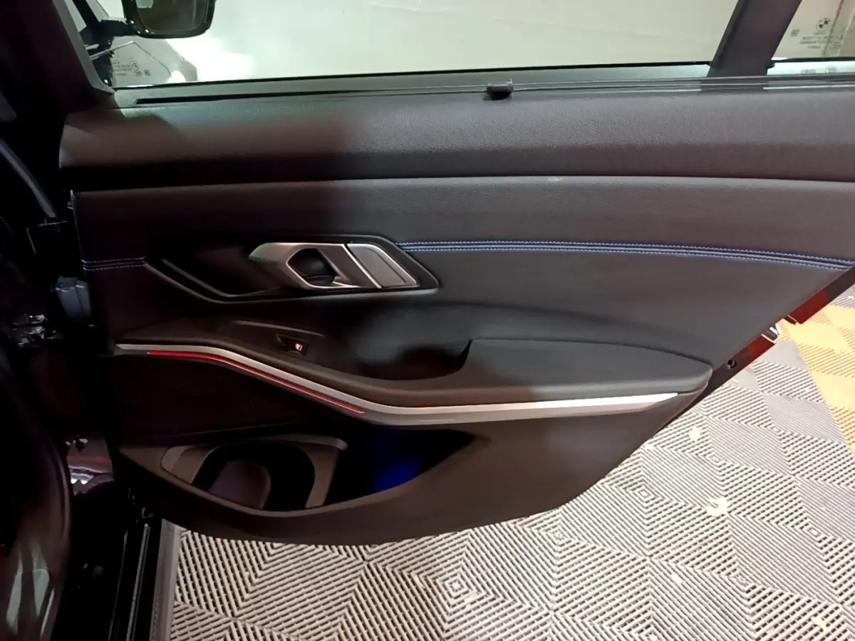 Vue rapprochée de la porte intérieure côté gauche noire de la BMW Série 3 318i M Sport avec éclairage d'ambiance rouge.