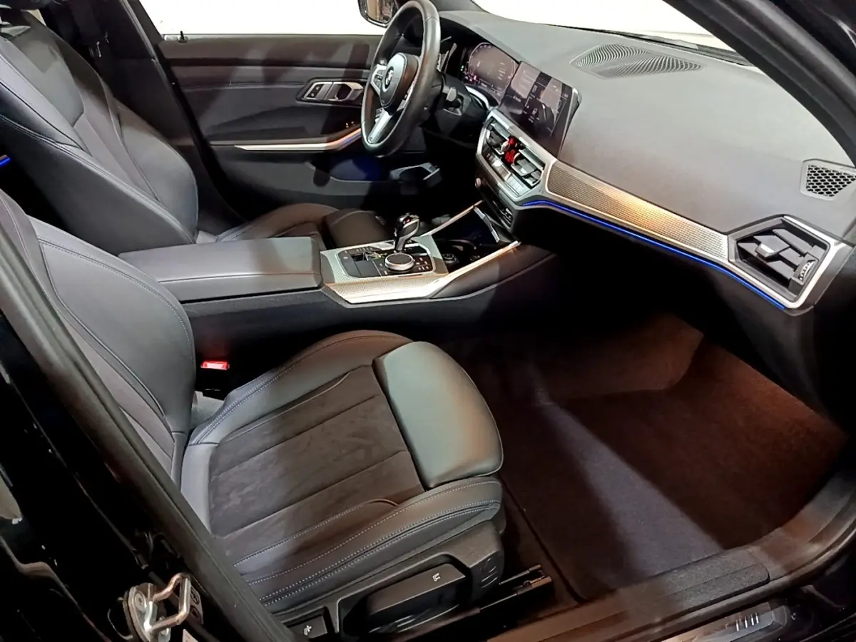 Intérieur noir de la BMW Série 3 318i 2022, vue côté conducteur, avec tableau de bord digital et éclairage d'ambiance bleu.
