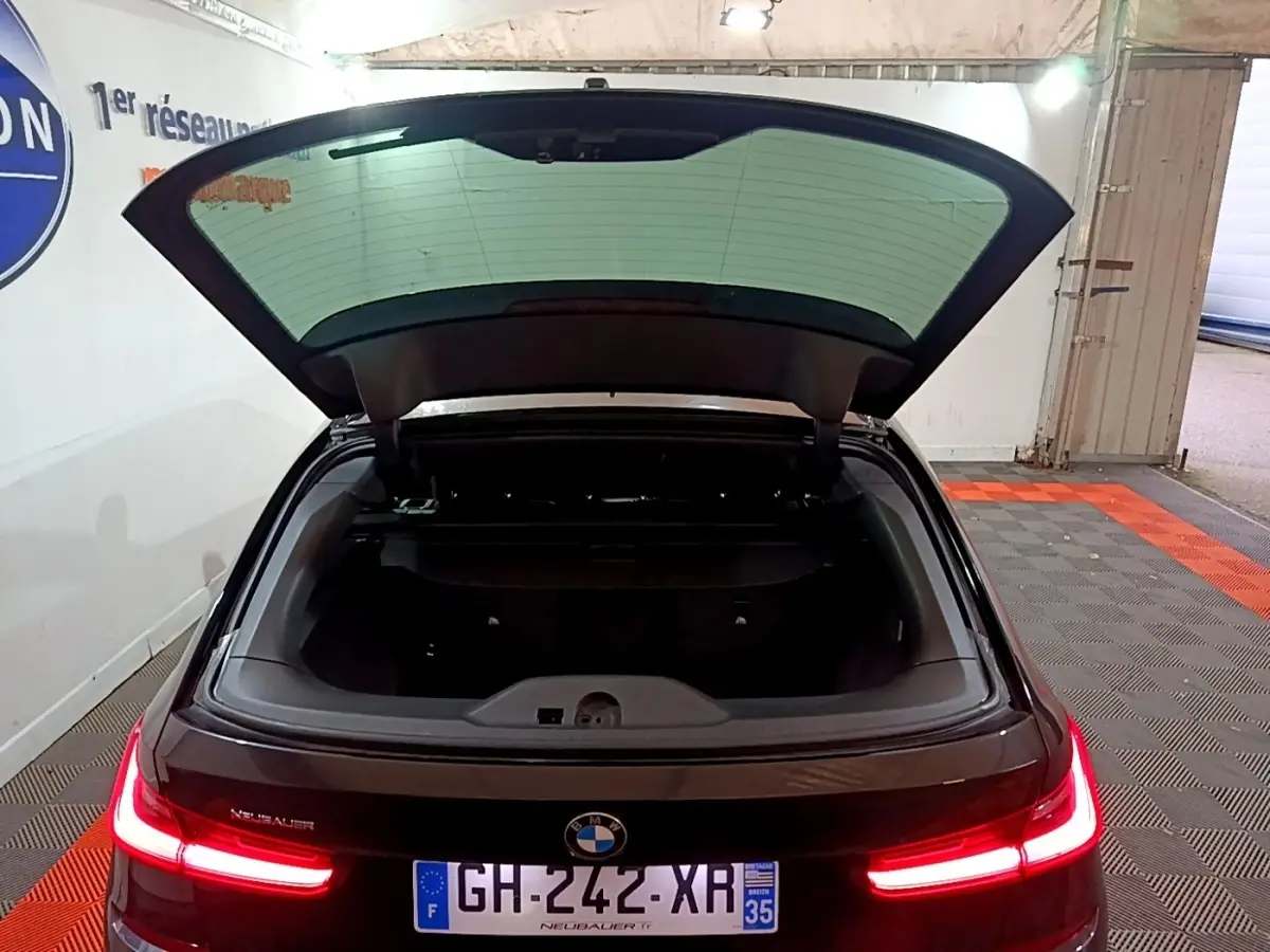 Vue arrière d'une BMW Série 3 noire 318i M Sport 2022 avec coffre ouvert et feux arrière LED allumés.