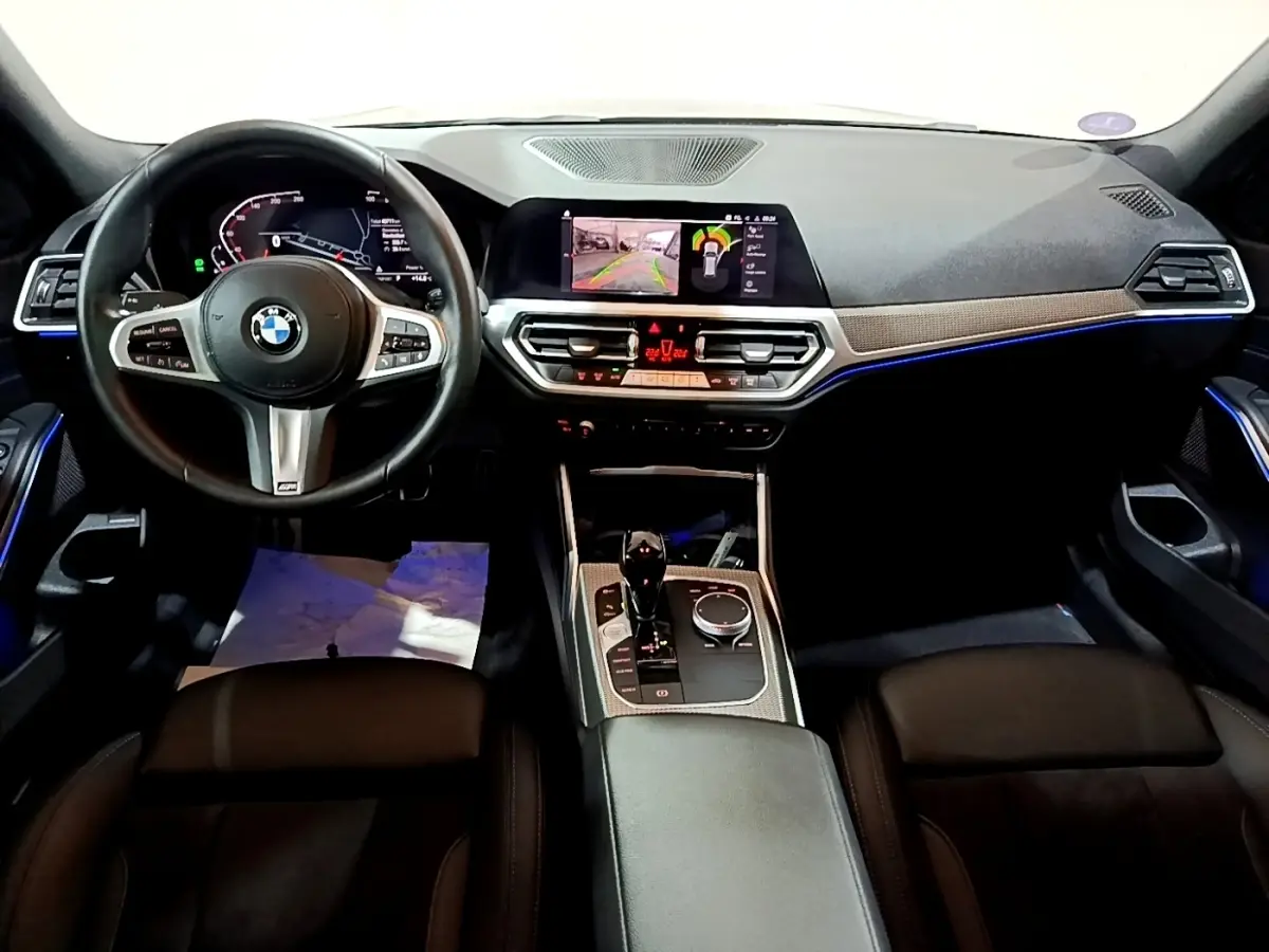 Vue intérieure avant de la BMW Série 3 318i M Sport 2022 avec tableau de bord numérique et éclairage d'ambiance bleu.