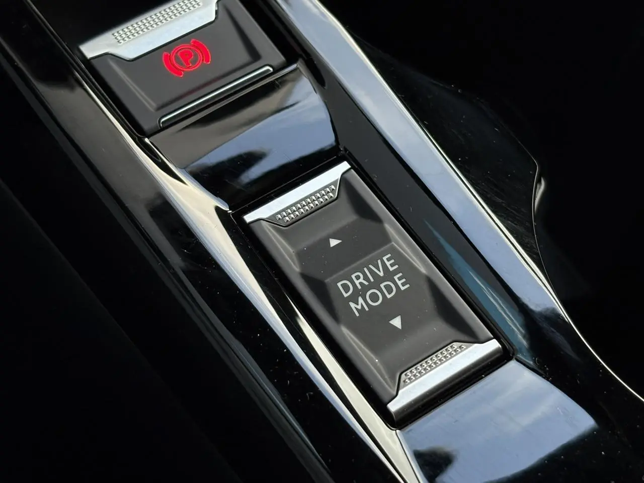 Gros plan sur la console centrale noire brillante du Peugeot 2008 Hybrid 145 e-DSC6 Allure avec bouton Drive Mode et frein électrique.