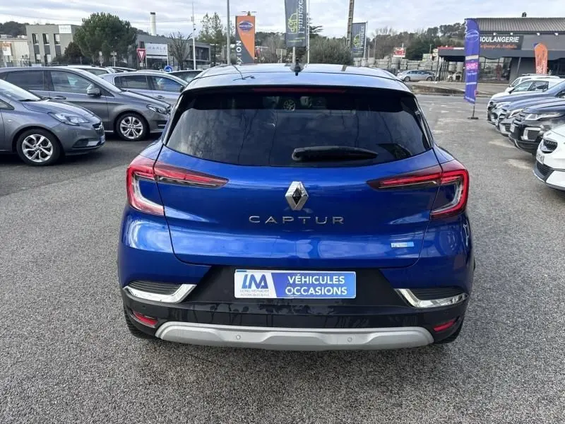 Vue arrière d’un Renault Captur bleu métal 2022 avec feux LED et logo centré sur un parking de voitures d’occasion.