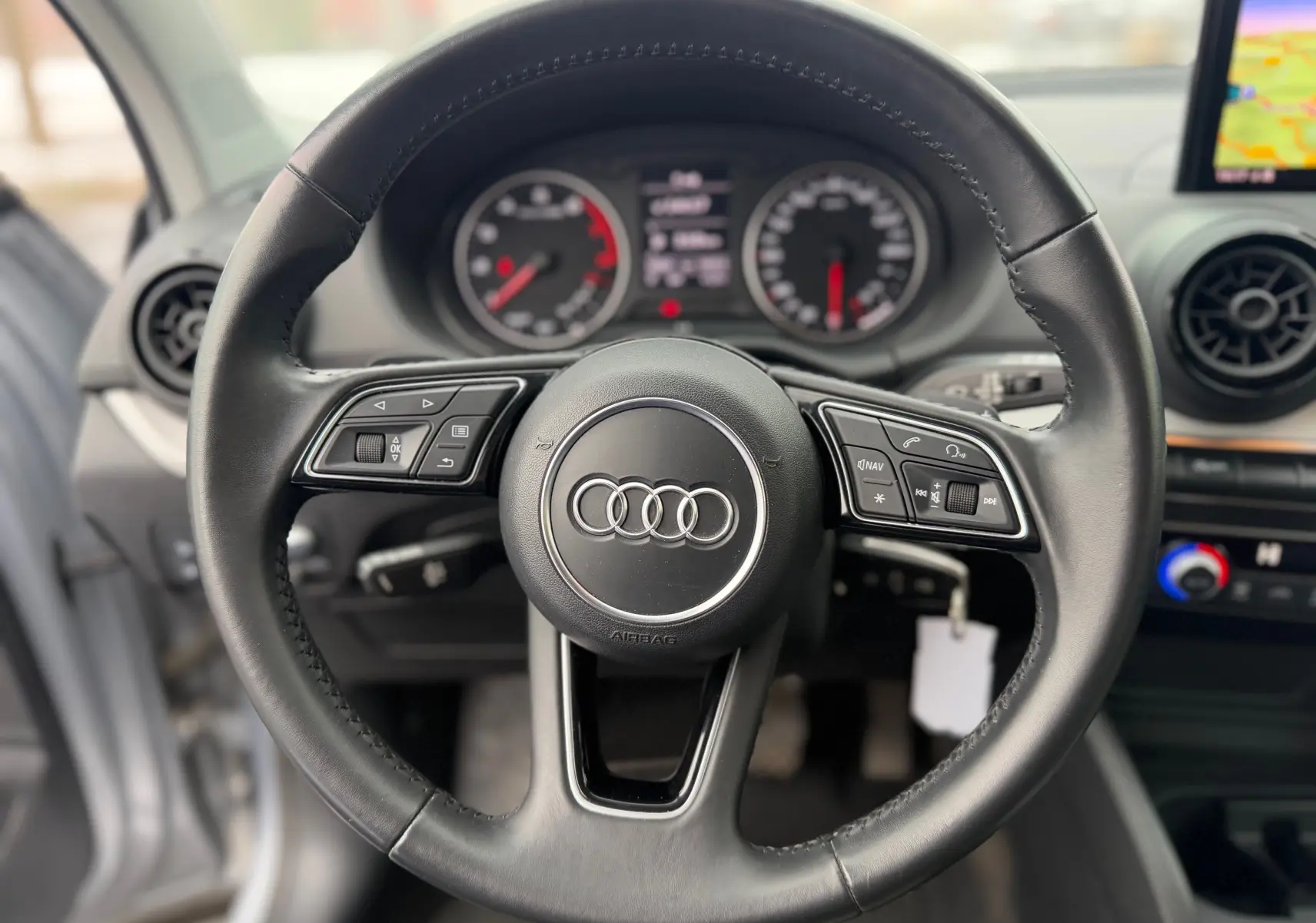 Vue rapprochée du volant en cuir noir de l'Audi Q2 2017 avec commandes multifonctions et tableau de bord en arrière-plan.