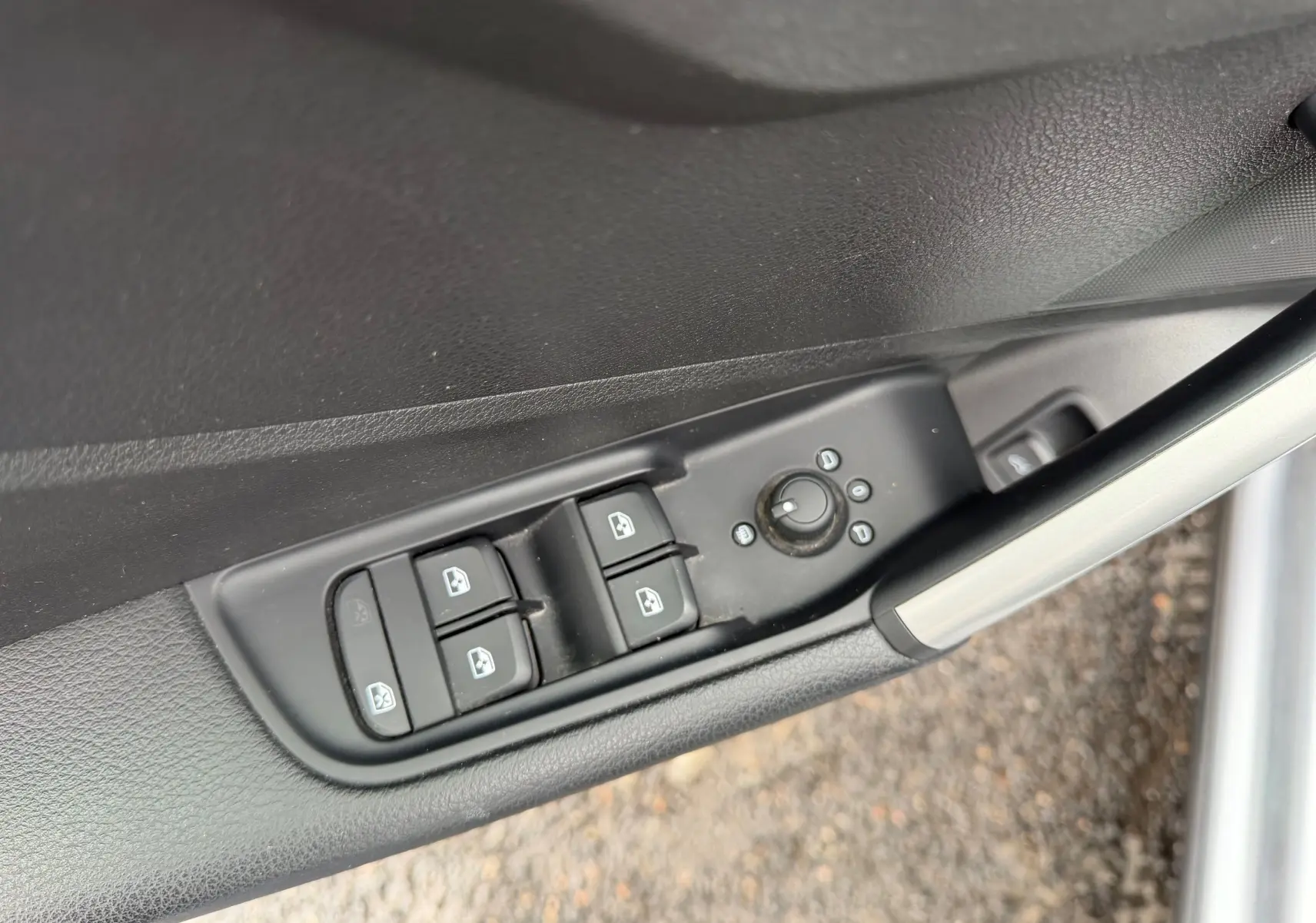 Gros plan sur les commandes de lève-vitres et réglage des rétroviseurs sur la porte côté gauche d’un Audi Q2 gris aluminium.