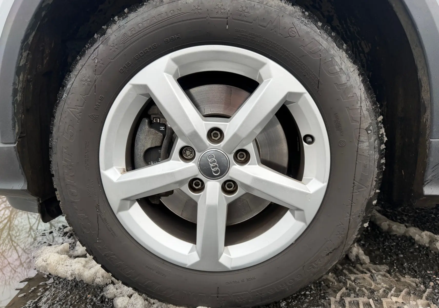 Gros plan sur la roue avant droite d'un Audi Q2 gris aluminium, avec jante alliage 5 branches et pneu hiver Dunlop.