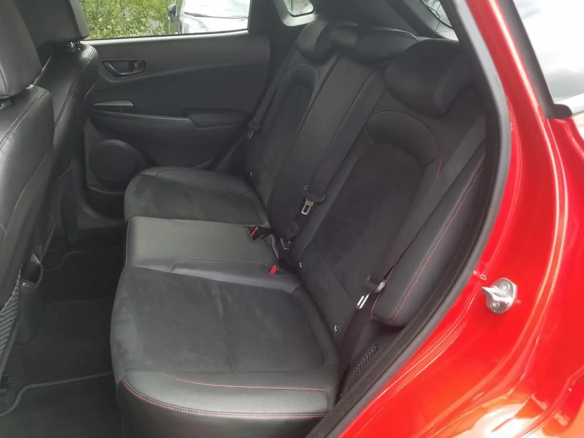 Vue intérieure côté arrière droit du Hyundai Kona rouge 2023, montrant les sièges arrière en Alcantara noir avec surpiqûres rouges.