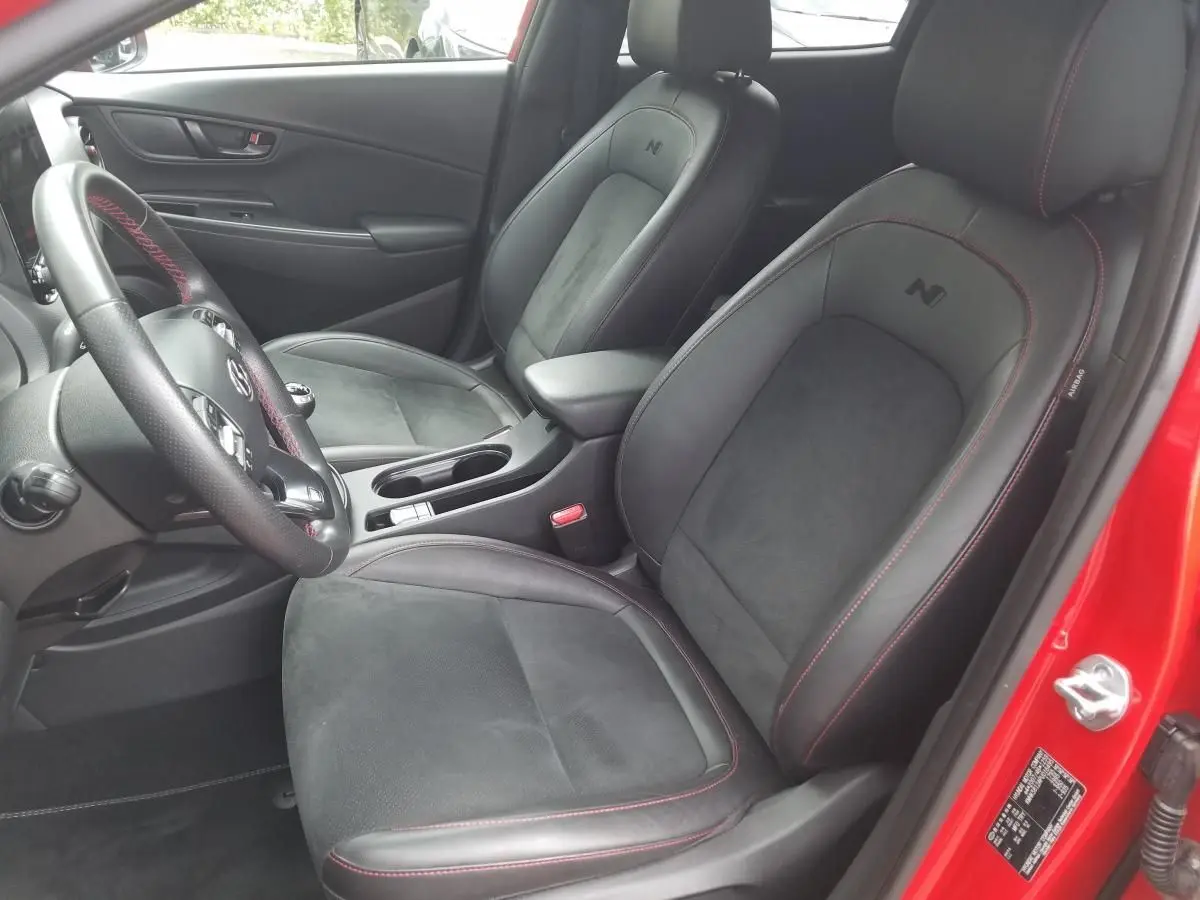Vue intérieure côté conducteur du Hyundai Kona rouge 2023 avec sièges N Line en Alcantara et cuir noir à surpiqûres rouges.