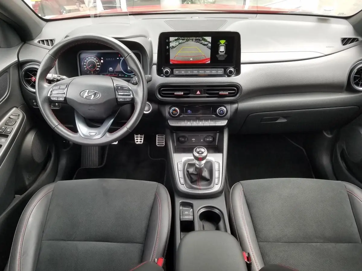 Vue intérieure avant du Hyundai Kona rouge 2023, tableau de bord moderne avec écran central et boîte manuelle.