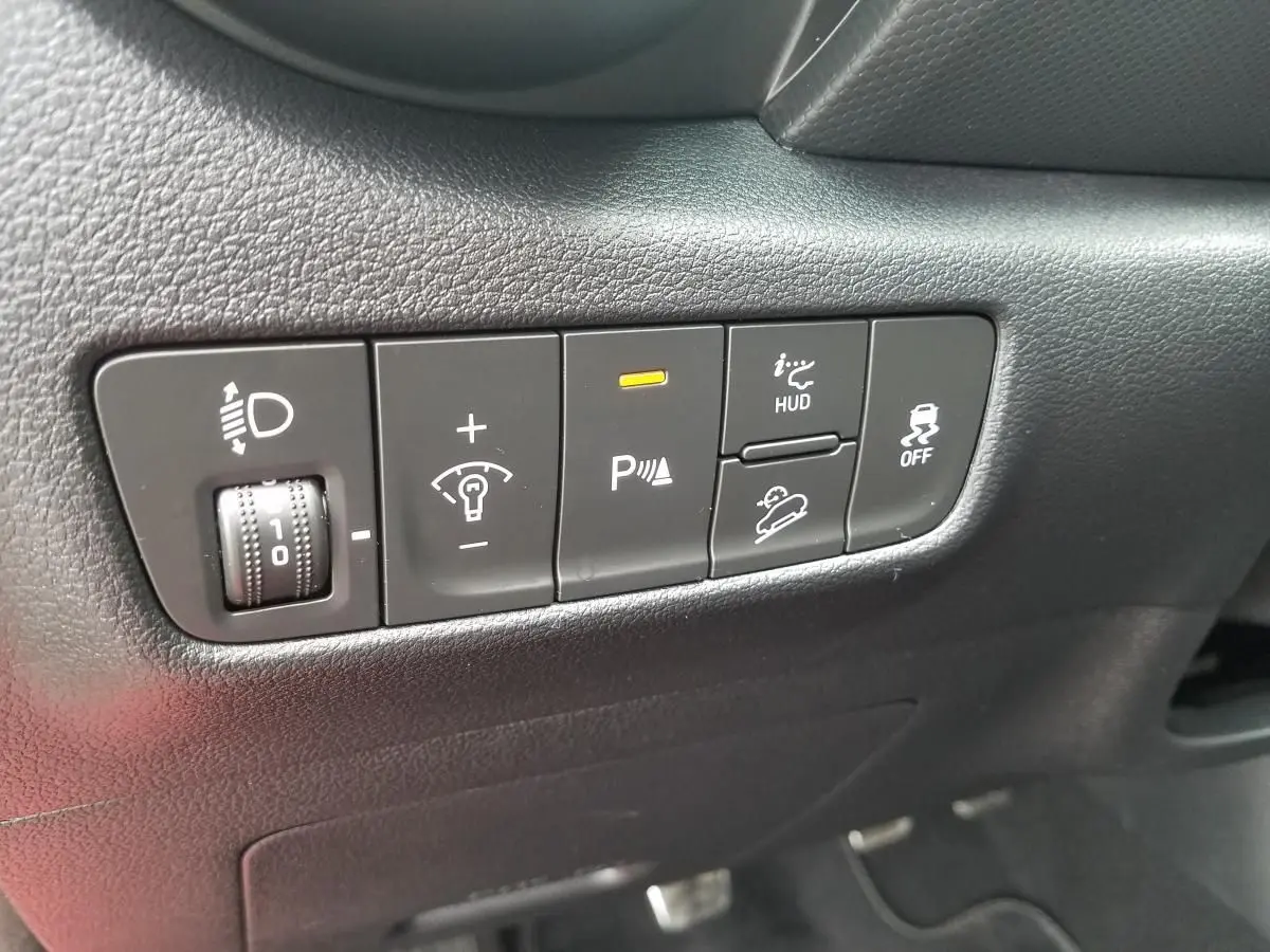 Gros plan sur les commandes intérieures noires du tableau de bord du Hyundai Kona rouge, avec bouton d'aide au stationnement activé.