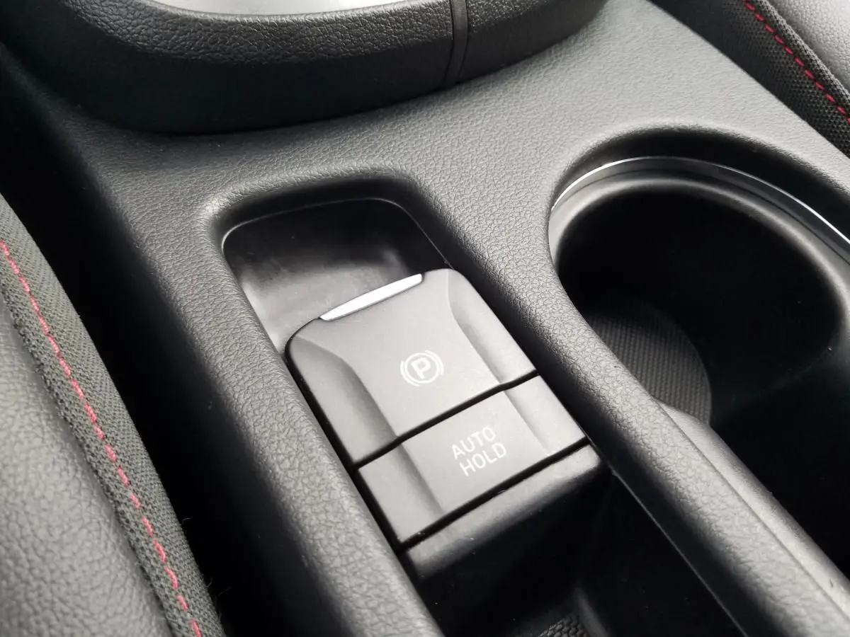 Gros plan sur la commande de frein de parking électrique et auto hold dans l’habitacle noir du Hyundai Kona rouge.