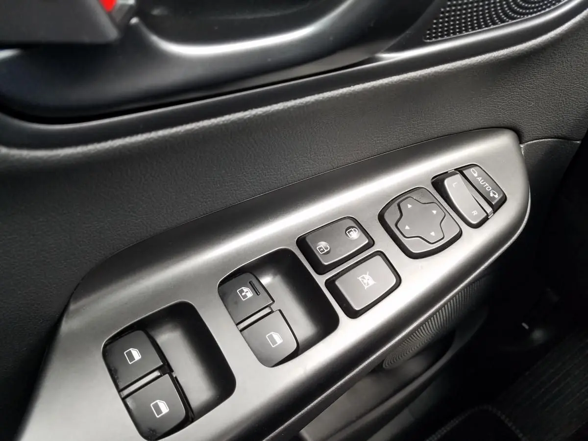 Gros plan sur les commandes de lève-vitres et rétroviseurs côté gauche intérieur du Hyundai Kona rouge 2023.
