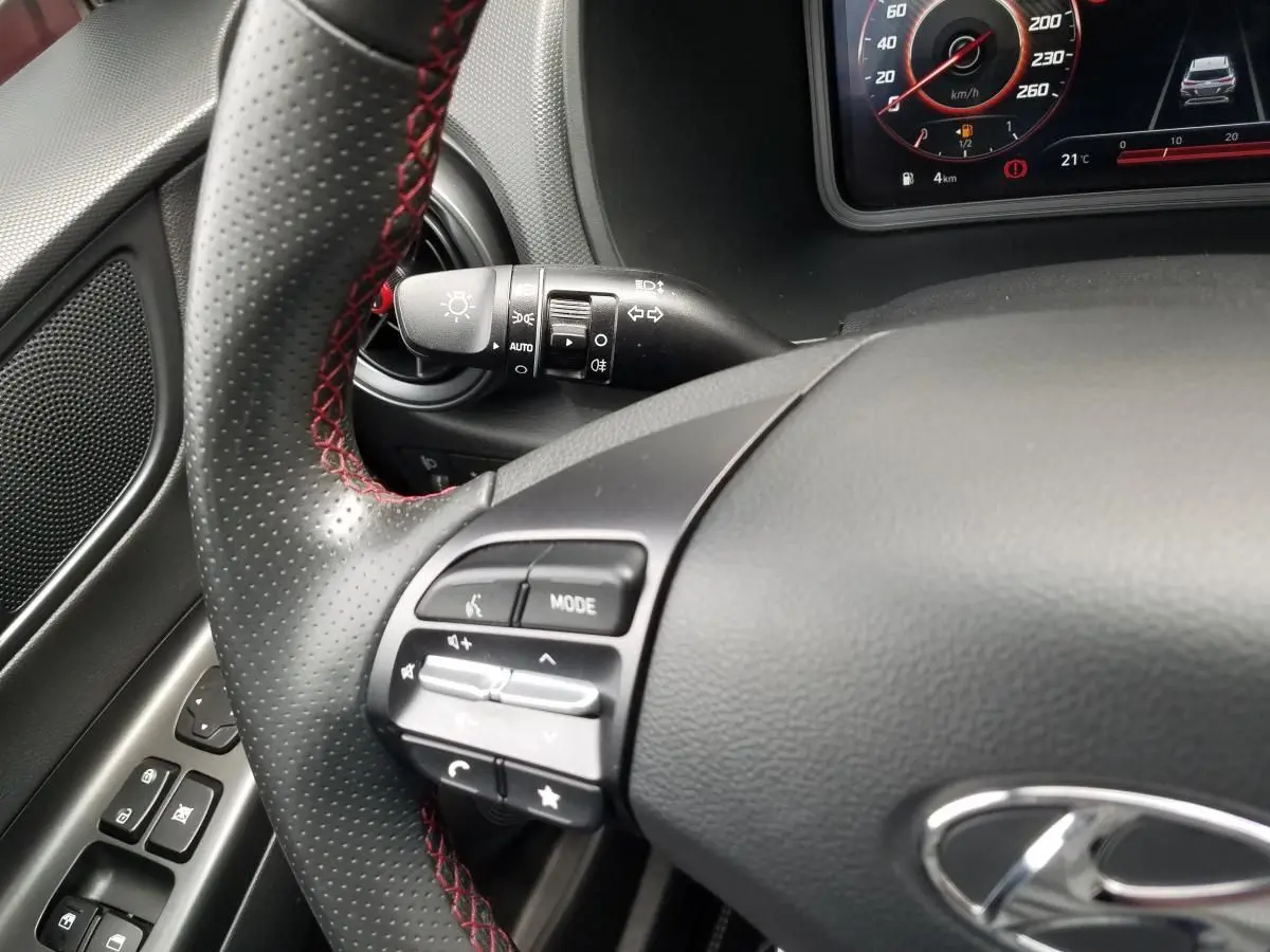 Gros plan sur le volant perforé avec surpiqûres rouges et commandes multifonctions du Hyundai Kona hybride 2023.