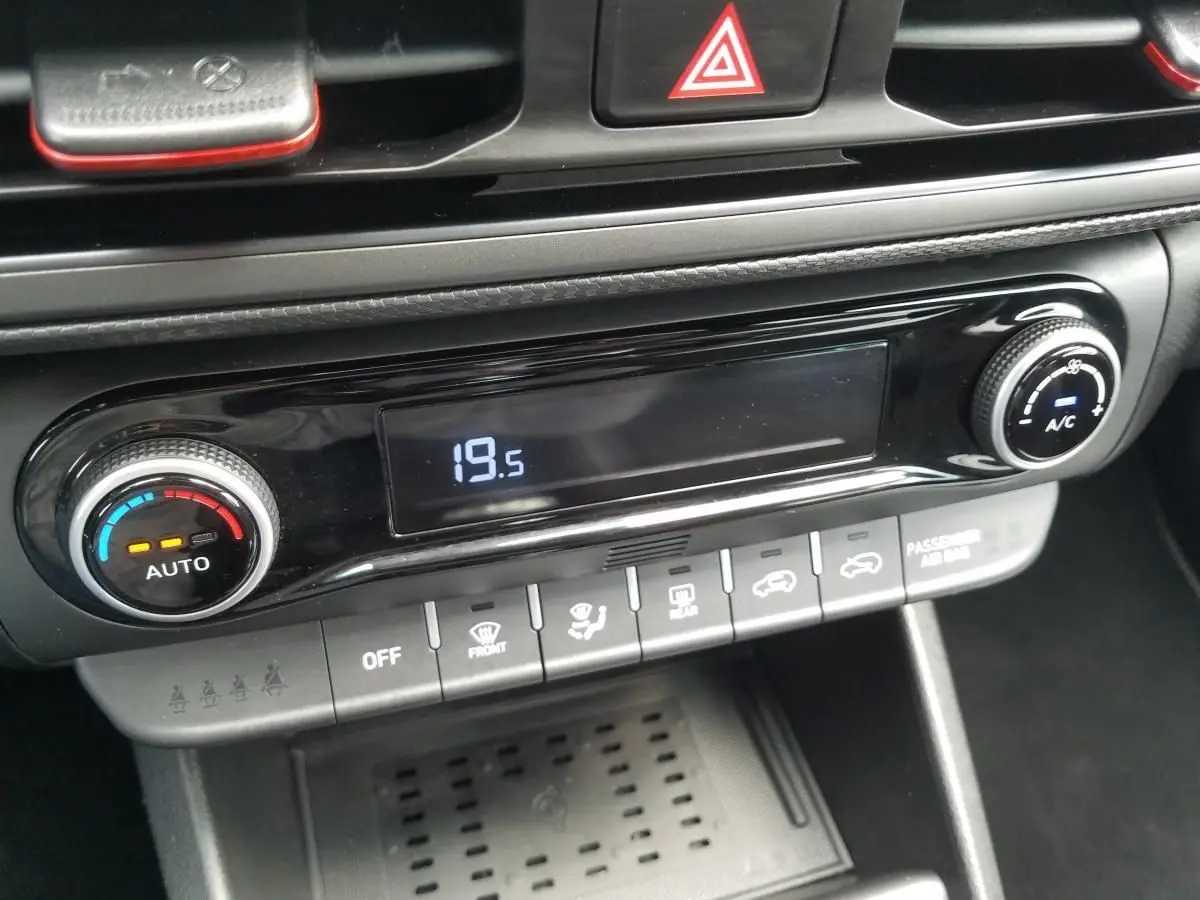 Gros plan sur la console centrale du Hyundai Kona rouge 2023, affichant la climatisation automatique à 19,5°C.