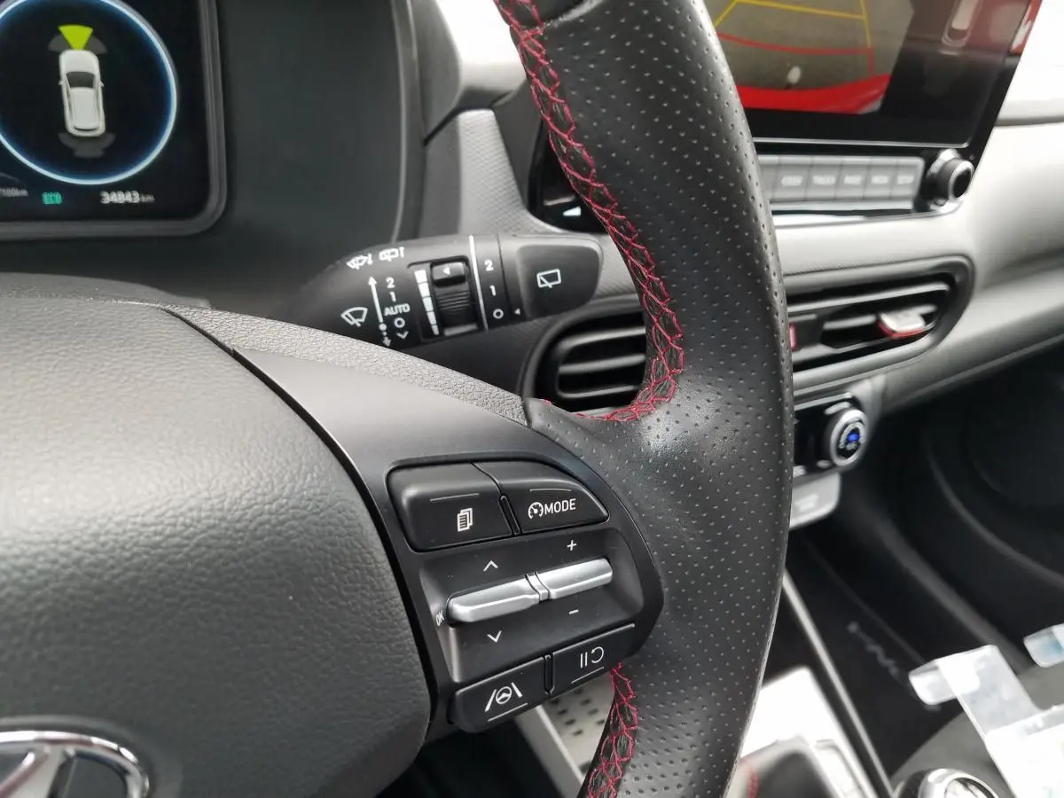 Gros plan sur le volant perforé avec surpiqûres rouges du Hyundai Kona hybride, tableau de bord et écran tactile en arrière-plan.