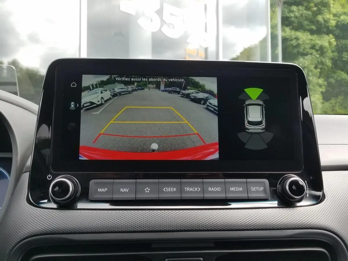 Écran central affichant la caméra de recul du Hyundai Kona rouge, avec guidage de stationnement et capteurs d'obstacles.
