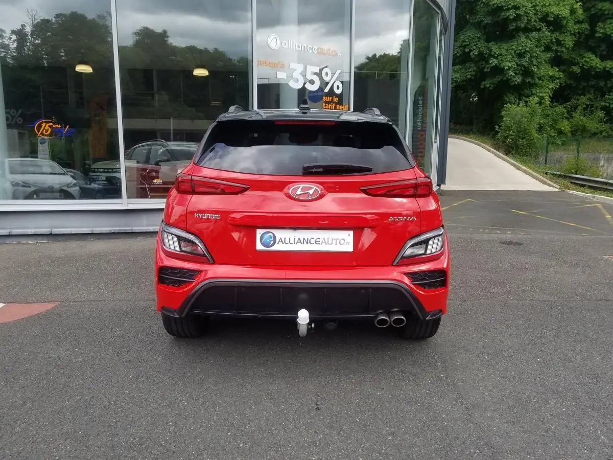 Vue arrière d'un Hyundai Kona rouge 2023 avec toit noir, double sortie d'échappement et attelage visible.